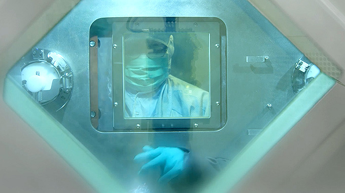 A person in a protective suit is in a glass enclosure.