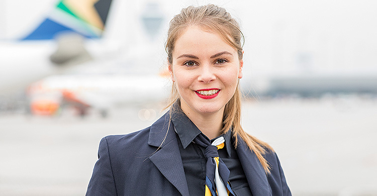 Eine Frau in Anzug und Krawatte steht vor einem Flugzeug.