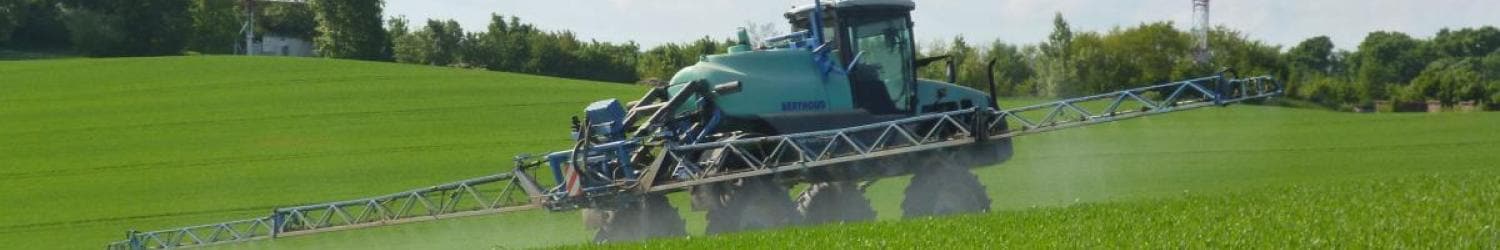 An einem sonnigen Tag ist ein Traktor mit einem großen Sprühaufsatz auf einem üppig grünen Feld im Einsatz.