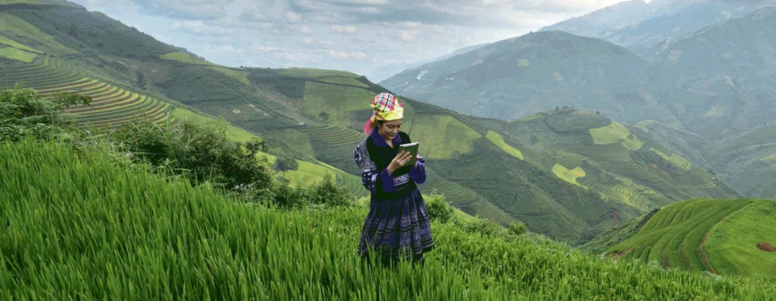 A woman is standing in a green field with mountains in the background.