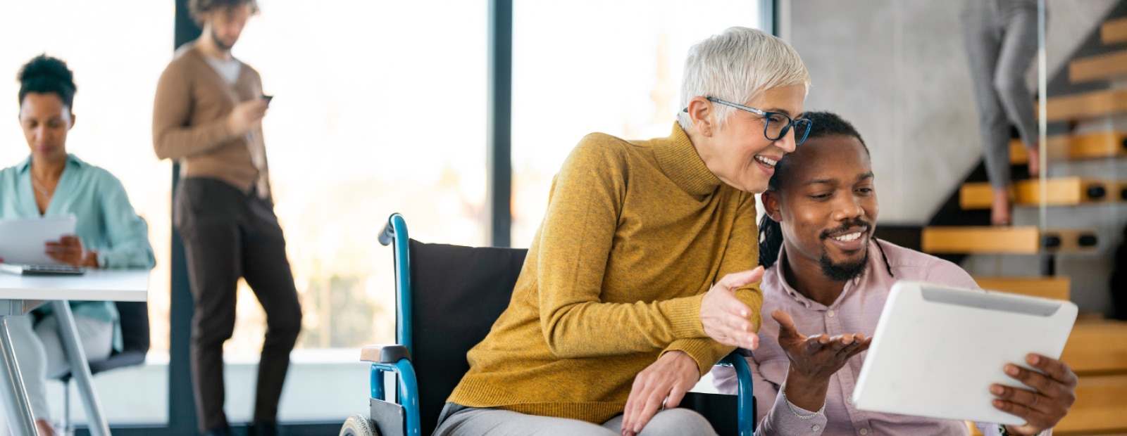 Senior woman in wheelchair with a man looking at a tablet.