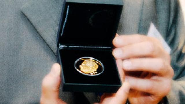 A man in a suit holding a gold medal.