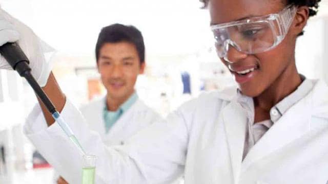 Two women in lab coats holding a test tube.