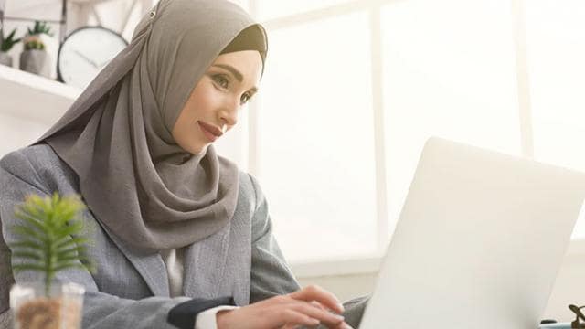 A muslim woman in hijab working on a laptop.