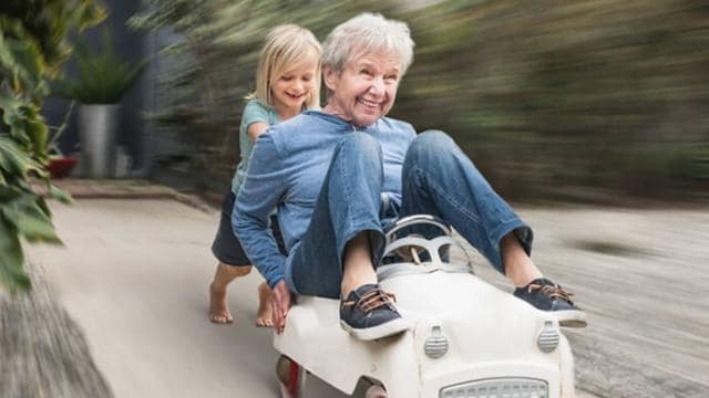 An elderly woman and her granddaughter riding on a toy car.