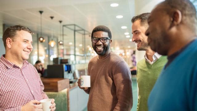 A group of men in a coffee shop talking to each other.