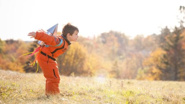 A young boy in an orange suit is standing in a field.