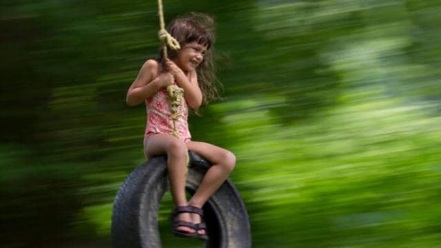 A little girl is swinging on a tire.