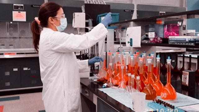 A woman wearing a lab coat and gloves is working in a laboratory.