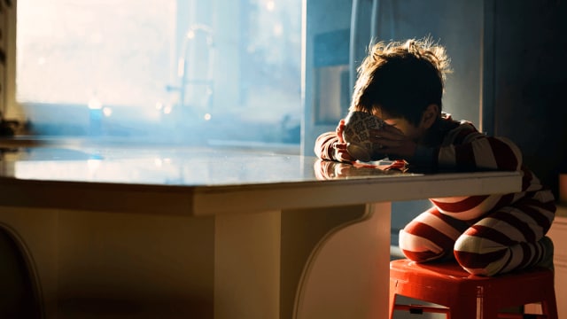 A child sitting on a stool in front of a window.