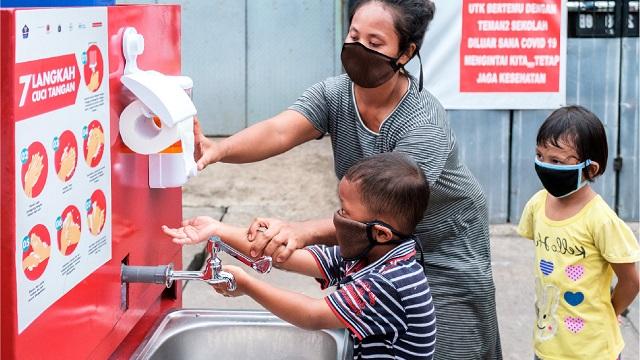 A woman and children are washing their hands at a vending machine.