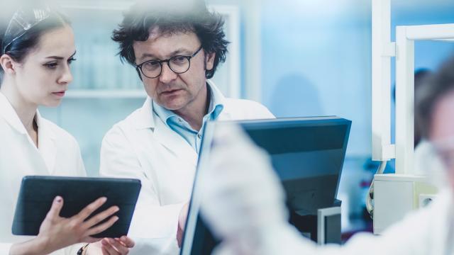 Two people in lab coats looking at a tablet.