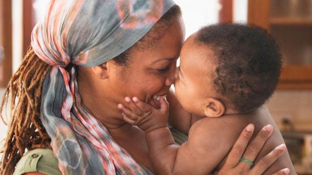 A woman kissing her baby in the kitchen.