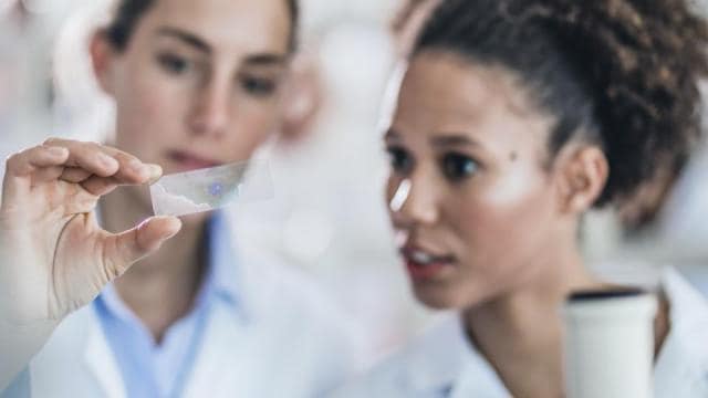 Two women in lab coats looking at a sample.