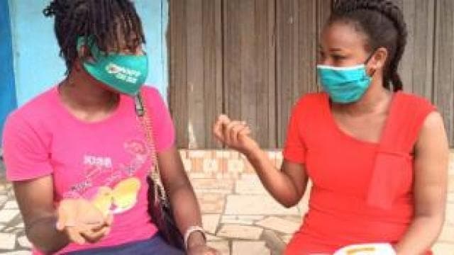 Two women sitting on the ground with face masks on.