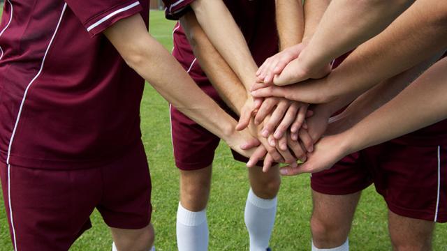 A group of soccer players putting their hands together.