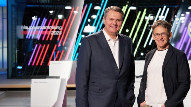 Two men in front of a stage smiling into the camera