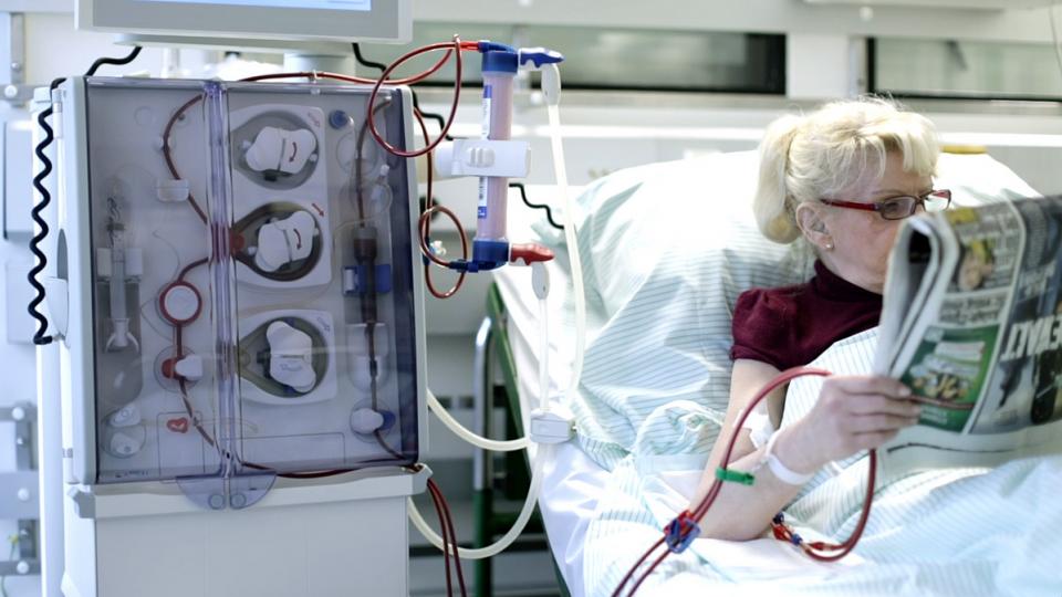 A woman in a hospital bed reading a newspaper.