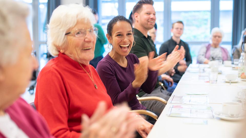 A group of elderly people clapping at a table.