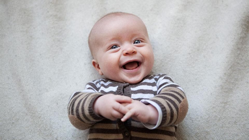 A baby is laughing while laying on a blanket.