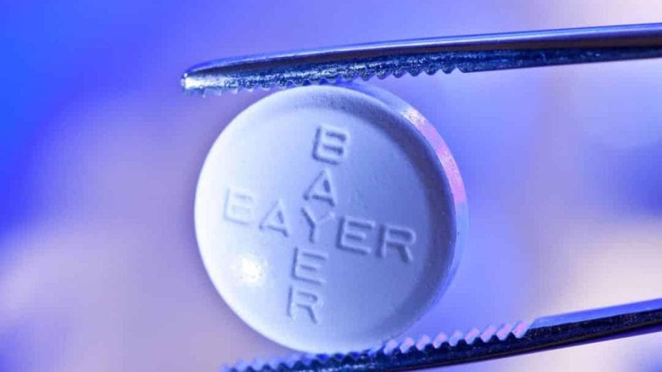 A tablet with the word bayer on it is being held by a pair of tweezers.