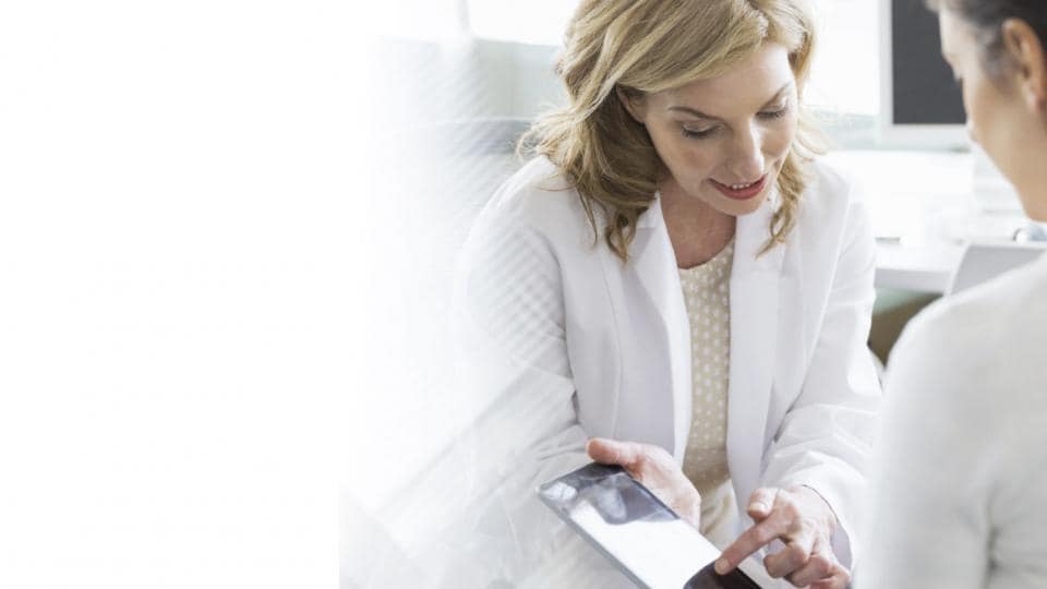 A woman is looking at a tablet while talking to a doctor.