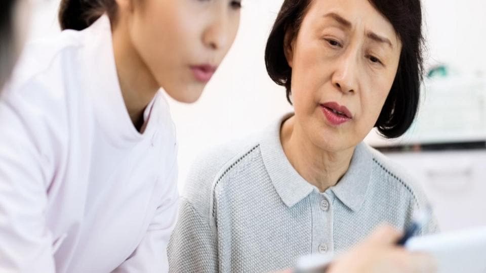 A woman is looking at a tablet while a doctor is talking to her.