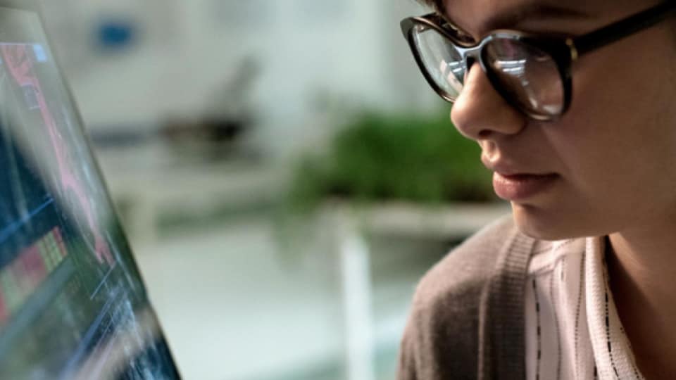 A woman wearing glasses is looking at a computer screen.