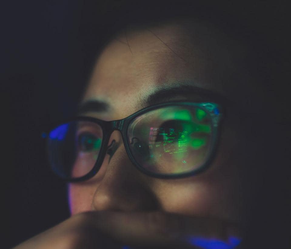 A woman wearing glasses with a green light on her face.