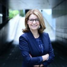 A woman in a business suit stands in a tunnel.