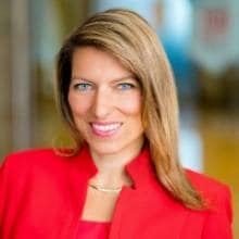 A woman in a red blazer smiles at the camera.