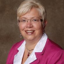 A woman wearing glasses and a pink jacket.