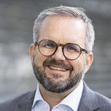 A man with glasses and a beard smiles into the camera.