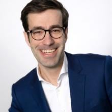 A man with glasses, a blue suit and a white shirt.