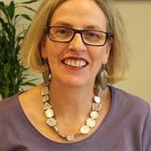 A woman with glasses and a purple shirt smiles.