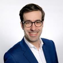 A man in a blue suit smiles at the camera.