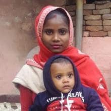 A woman is holding a baby in front of a house.