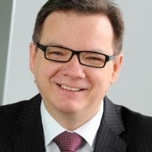 A man in a suit and tie smiles at the camera.