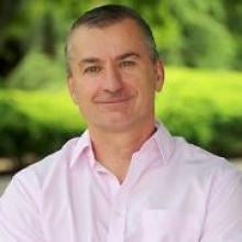 A man in a pink shirt stands in a park.