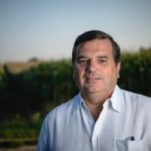 A man in a white shirt stands in front of a corn field.