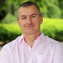 A man in a pink shirt with his arms crossed.