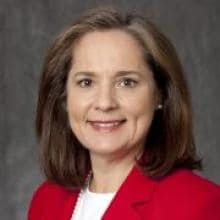 A woman wears a red blazer and white pearls.