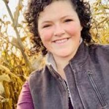 A woman stands in a corn field.