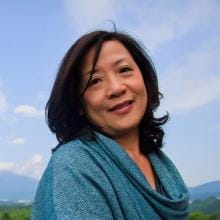 A woman wearing a blue scarf in front of a mountain.