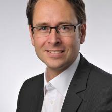 A man wearing glasses and a suit is posing for a photo.