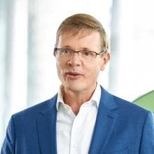 A man in glasses is standing in front of a green wall.